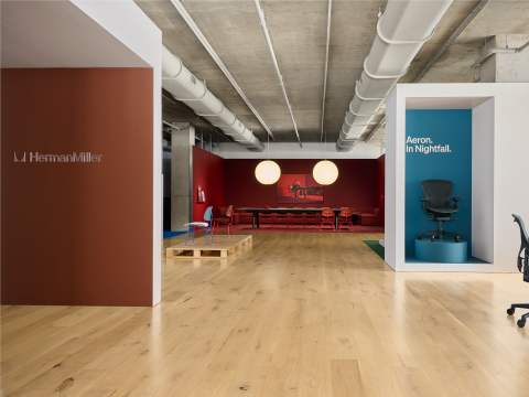 A wide view of showroom with areas differentiated by brown, red, and white walls and a blue Aeron office chair set into a blue alcove.
