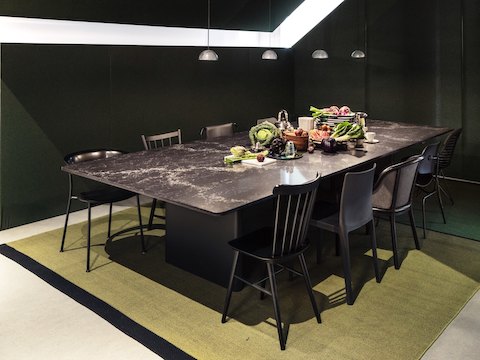 A dining room with a Geiger Axon table with black marble top, a pile of fruits and vegetables in the center of the table, and an assortment of side chairs around the table, all in black.
