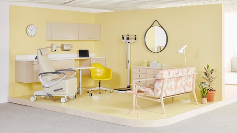 A workplace exam space with bright yellow walls, Mora System wall-mounted workstation, a yellow Eames Task Chair on casters, an Ava Recliner, and a Palissade Settee with pink pattern upholstery.
