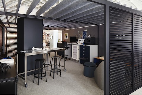 A maker studio created with Overlay with dark gray walls, a stainless steel Quovis Standing-Height Table, black Revolver Stools, a Procedure Cart with Meridian Storage, and a Hay About a Chair in the corner.