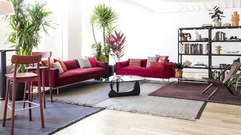 A red Bolster sofa and settee anchor a residential setting that includes stools, plants, and bookshelves.