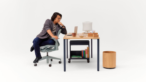 Ein Mann sitzt in einem Bürostuhl in drei verschiedenen Positionen und tippt auf einem Laptop auf einem Schreibtisch. 