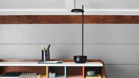 Slim black task lamp on a desk, placed alongside pens and stationery.