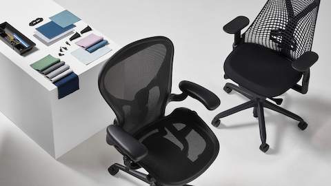 A black Aeron and Sayl office chair viewed from above, are positioned next to a white display cube, on top of which an arrangement of folded Revenio textile swatches, OE1 trolly plastic clips, and a Tu Pedestal Utility Tray made from ocean-bound plastics are all displayed.