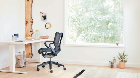 Cosm Chair seen from a side view at a Motia Sit-Stand Desk in a bright room.