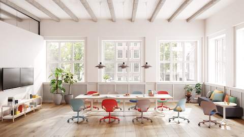 A meeting space featuring nine Zeph chairs in red, light blue and light brown that surround a Headway table. and round side table.