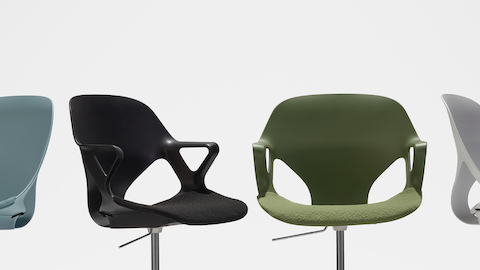 Four Zeph chairs in a row turned at different angles and focused on their seats. There is a light blue armless chair, black chair with fixed arms, olive chair with fixed arms and a light grey armless chair.