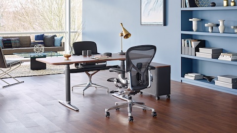 An executive office featuring a height-adjustable desk with a black Aeron Chair and a sitting area with a Tuxedo Sofa and Sled Chair.