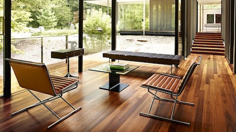 A bright seating area with floor-to-ceiling windows, two Sled Chairs, and a Tuxedo Bench. Select to learn about The Herman Miller Collection.