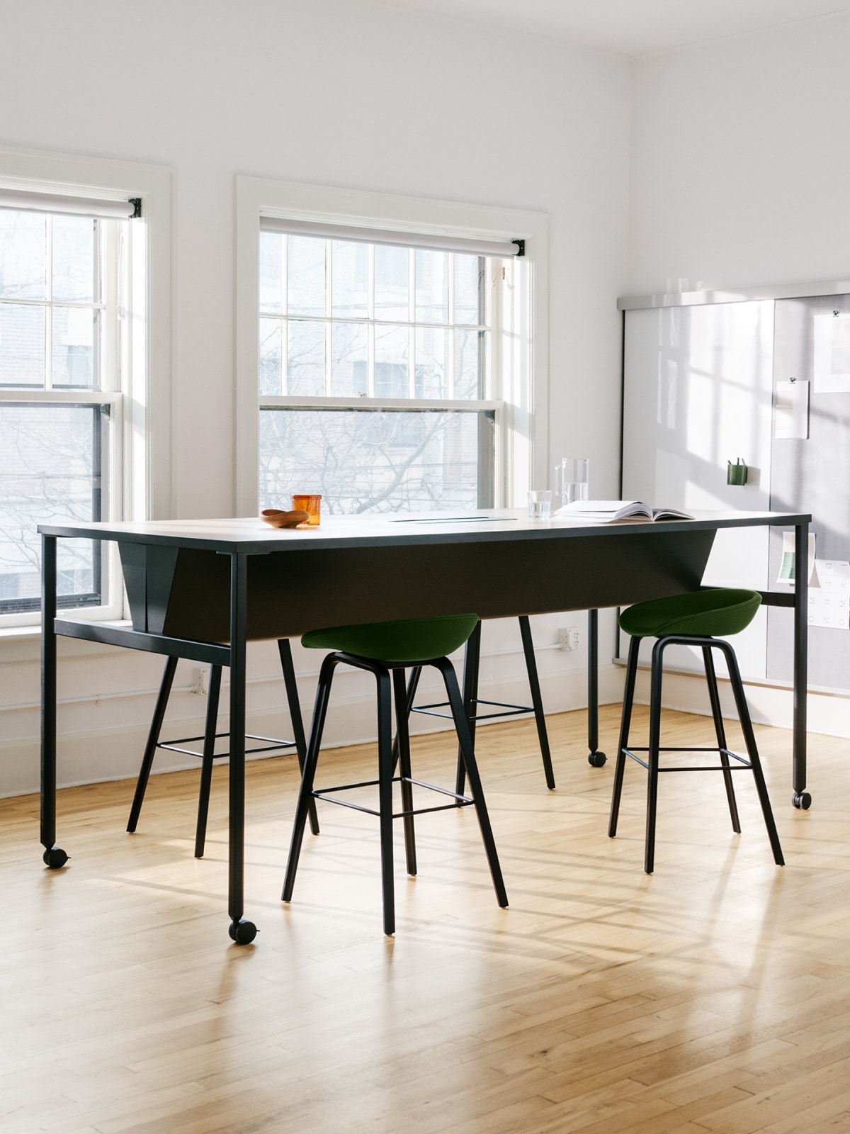 A black double sided OE1 Communal Table with casters, and OE1 Wall Rail and Board in the background of a large bright conference room.