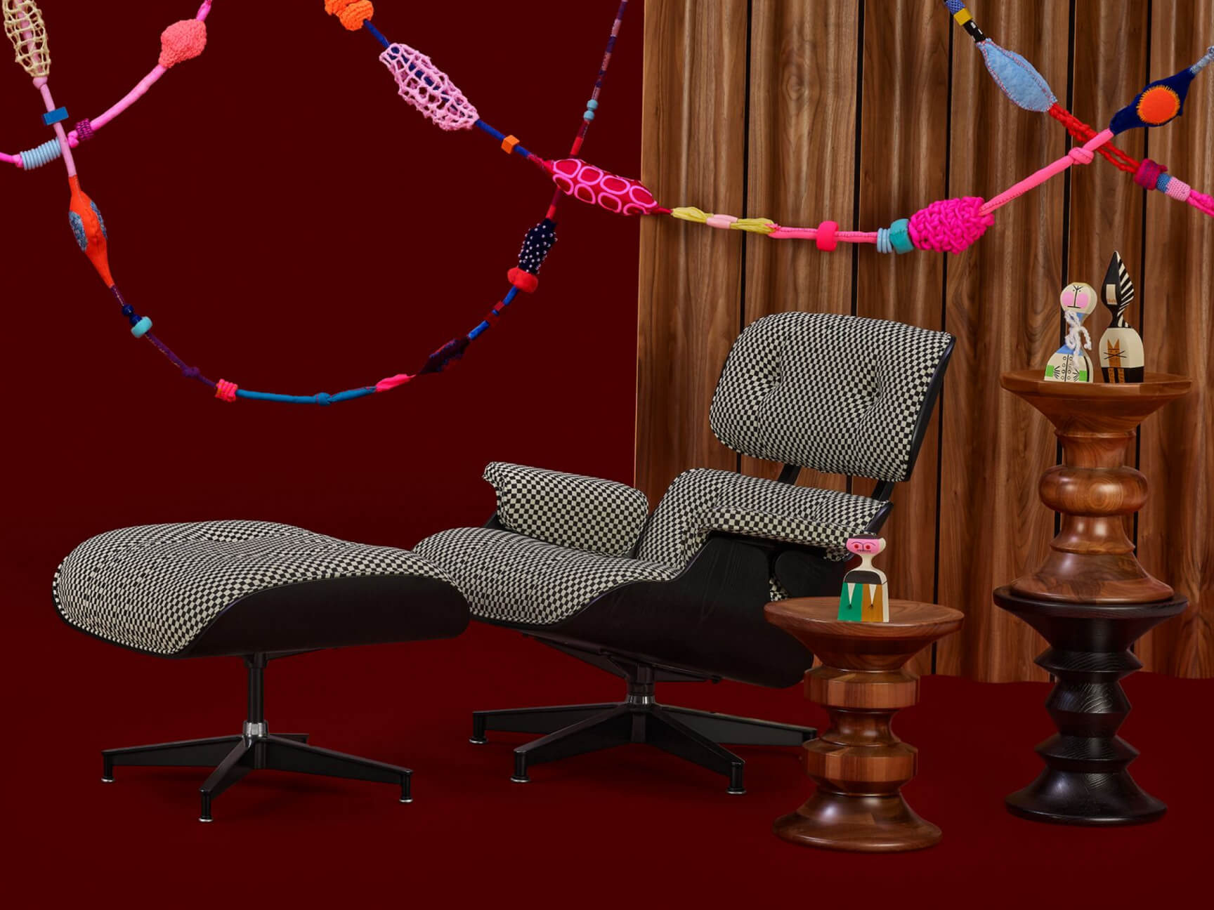 An Eames Lounge Chair and Ottoman is featured below colorful streamers with Eames Turned Stools and Girard Wooden Dolls next to it.