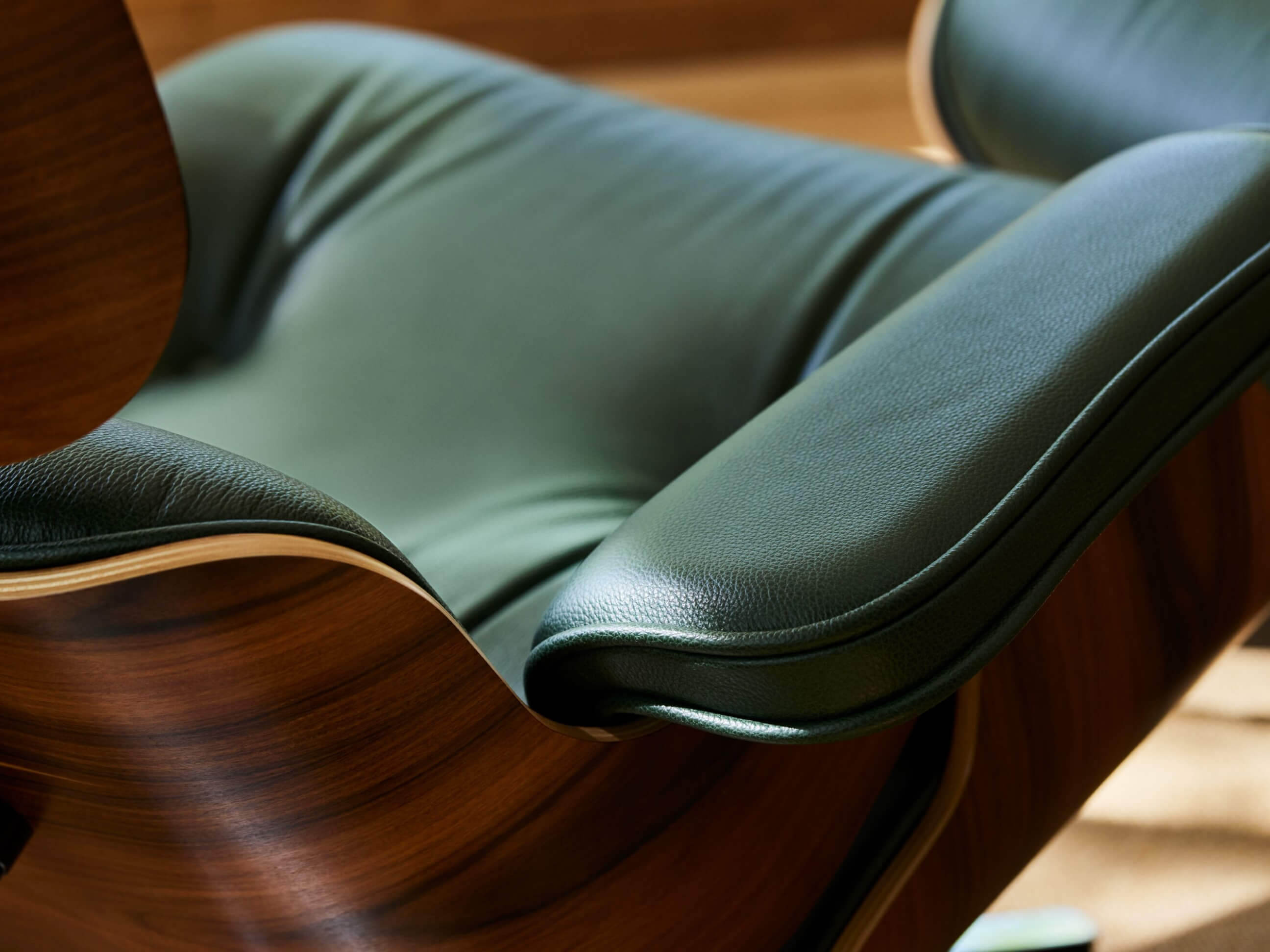Close-up of an Eames Lounge Chair’s green leather upholstery and the elegantly curved wood shell.