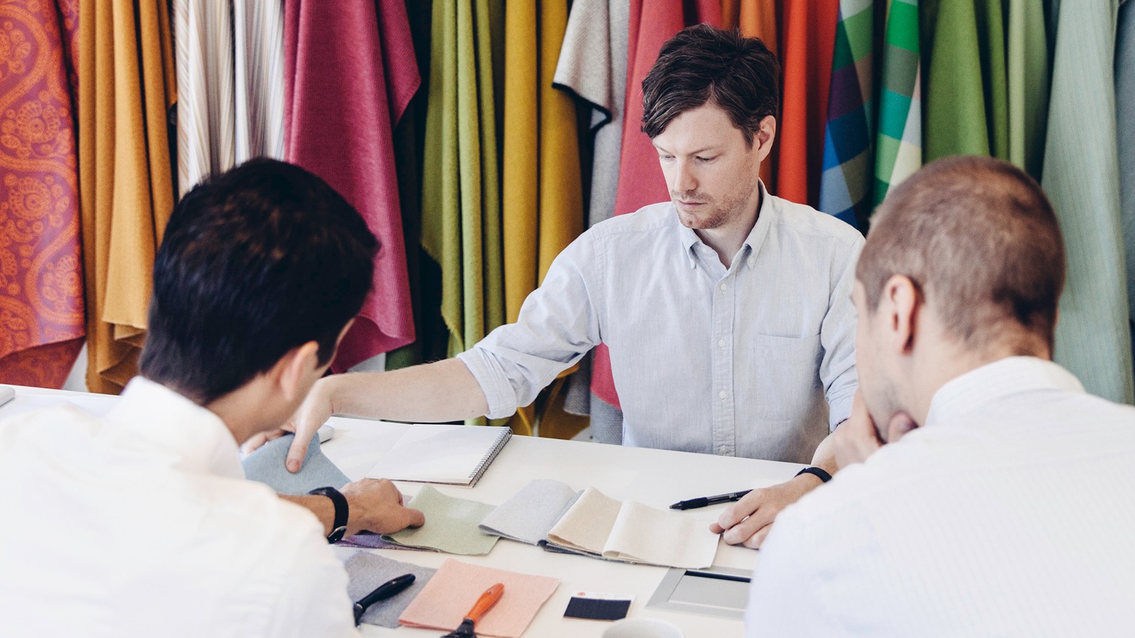 Four seated men review fabric samples.