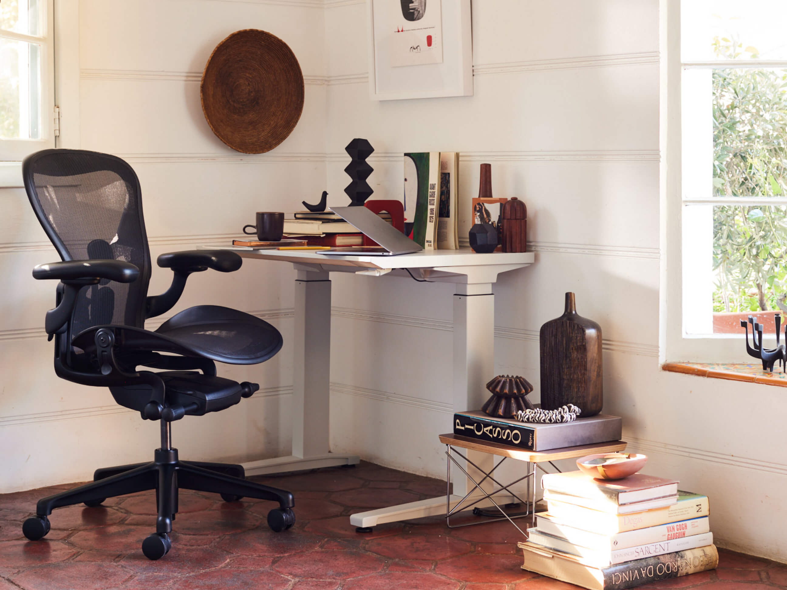 An ergonomic and personalized home office in a brightly lit corner, decorated with vases and books.