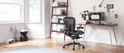 An AbakEnvironments Desk with a walnut top and polished legs, with a graphite Aeron Chair in a light home office setting and Folk Ladder Shelving.