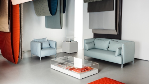 A pastel blue ColourForm lounge chair and sofa beneath hanging textiles of various colors.