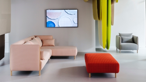 Three ColourForm seating pieces—pink sectional, red ottoman, and gray lounge chair—beneath hanging textiles in shades of green.