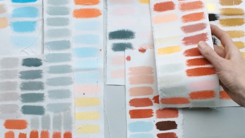 Sheets of color samples on a work surface; a hand picks up one.