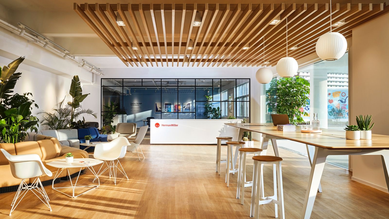 A plaza in the Dongguan facility showroom, featuring lounge seating, an Optimis high table with stools, and three Nelson pendant lights.