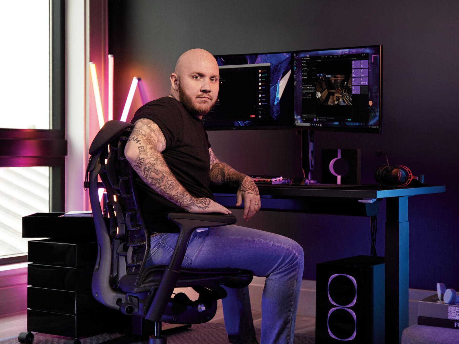 Een man die een koptelefoon draagt zit in een Gaming-stoel, is gericht naar een opstelling met een gamingtoetsenbord, muis en twee schermen.