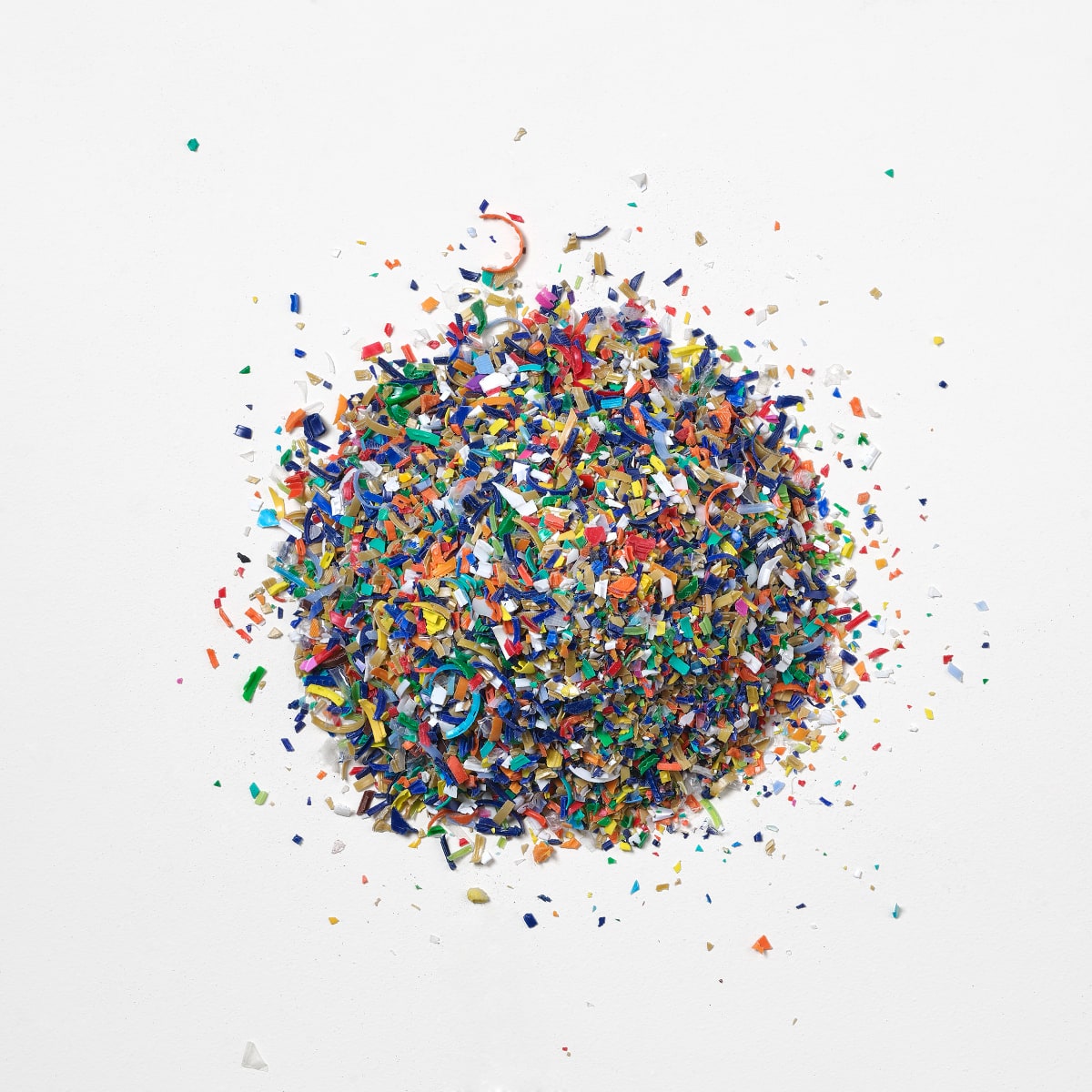 Ein runder Haufen und verstreute Teile von mehrfarbigem, recyceltem, gemahlenem Ocean Bound Plastic auf einem weißen Hintergrund. Ein runder Haufen und verstreute Teile von mehrfarbigem, recyceltem, gemahlenem Ocean Bound Plastic auf einem weißen Hintergrund.