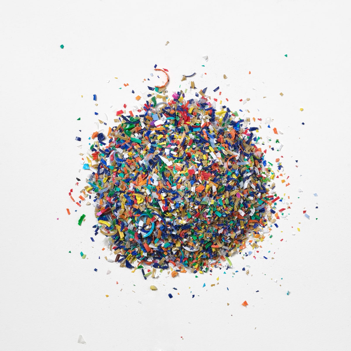 A round pile and scattered bits of multi-coloured recycled ocean-bound plastic flakes on a white background.