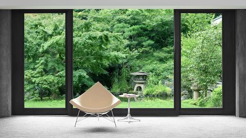 ネルソンペデスタルテーブルの隣りに置かれたライトファブリックのネルソンココナッツラウンジチェア。背景に日本庭園が見える