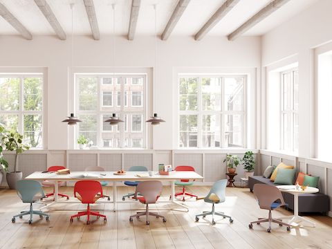 A meeting space featuring nine Zeph chairs in red, light blue and light brown that surround a Headway table and round side table.