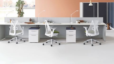 White Sayl chairs with green upholstered seats at an Action Office bench with storage pedestals and Action Office private offices nearby. 