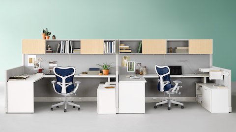 Dos estaciones de trabajo Action Office con paneles de tela grises, unidades de almacenamiento blancas y sillas de escritorio ergonómicas Mirra 2 azules.