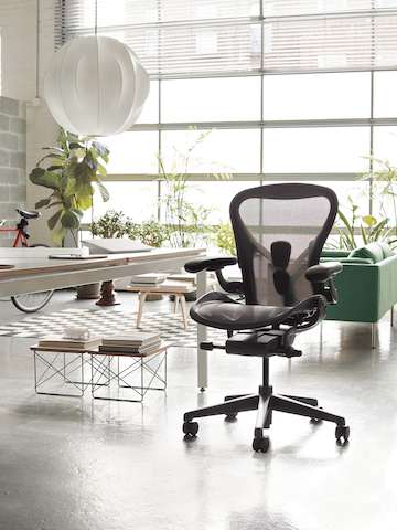 A black Aeron Chair in a sunny room with plants in the background, and pendant lighting.