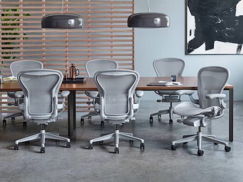 Seis cadeiras Aeron com acabamento mineral em torno de uma mesa de reuniões em imitação de madeira.