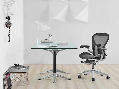 Zwarte ergonomische bureaustoel Aeron met gepolijste aluminium voet op een Burdick Group-tafel met glazen blad.