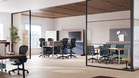 A collaborative space featuring four Aeron stools in dark grey around a table with monitor and four Setu chairs around a meeting table.