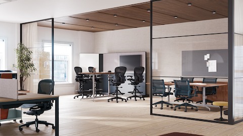 A collaborative space featuring four Aeron stools in dark grey around a table with monitor and four Setu chairs around a meeting table.