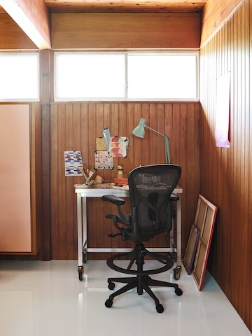 An Aeron Stool behind a metal desk in a wood-paneled workspace.
