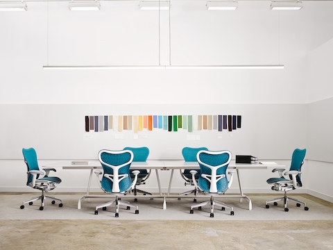 Le sedie da ufficio blu Mirra 2 circondano un tavolo rettangolare AGL con campioni di colore sulla parete dietro.