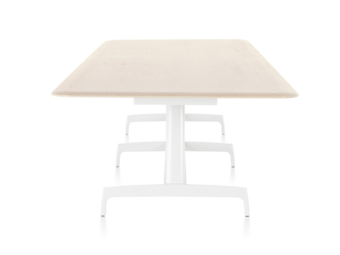 Ein langer rechteckiger AGL-Tisch mit einer hellen Furnierplatte und einer weißen Aluminiumbasis, vom schmalen Ende aus betrachtet.