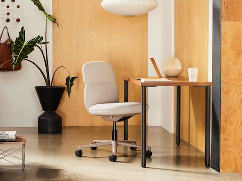 Silla Asari con respaldo medio de Herman Miller color crema en una habitación con paneles de madera, con mesa rectangular OE1 y sofá Wilkes color crema.