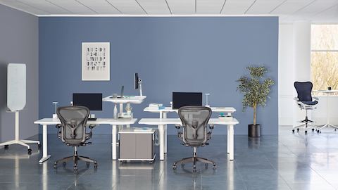 Een samenwerkingsgebied met witte, in hoogte verstelbare Atlas Office Landscape-bureaus en zwarte Aeron-bureaustoelen.