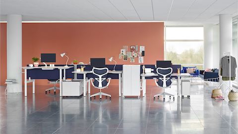 Une configuration de bancs ouverts avec des tables Atlas Office Landscape réglables en hauteur à différentes hauteurs et des chaises de bureau Mirra 2 bleues.