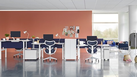 Une configuration de bancs ouverts avec des tables Atlas Office Landscape réglables en hauteur à différentes hauteurs et des chaises de bureau Mirra 2 bleues.