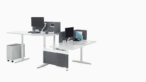 In hoogte verstelbare Atlas Office Landscape-desks in een configuratie van 90 graden, één op stahoogte en één op zittende hoogte.