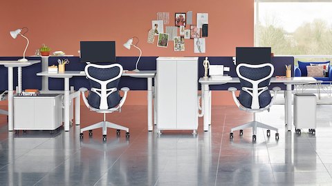 An open benching setup with height-adjustable Atlas Office Landscape desks at different heights and blue Mirra 2 office chairs.