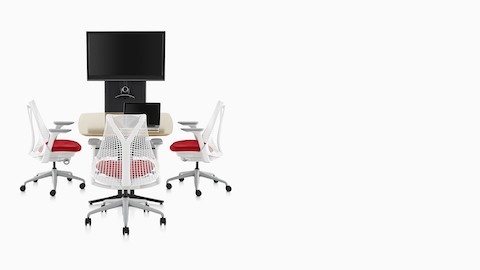 Três cadeiras de escritório ergonômicas Sayl com costas e molduras brancas e assentos estofados vermelhos em torno de uma mesa voltada para um carrinho de tecnologia AV / VC One.