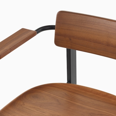 A close up of a Betwixt Chair with walnut backrest, seat, and arms.