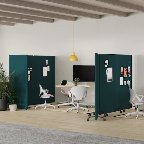An open office setting with three collaborative spaces with tables, chairs and monitors, separated by green Bound Freestanding Screens and Bound Mobile Screens.