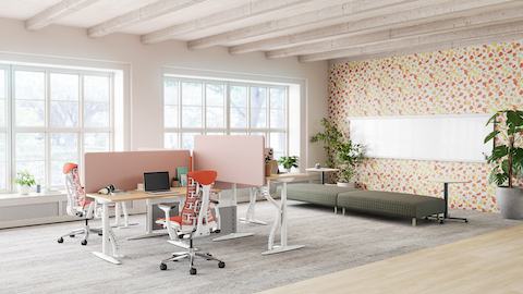 Ufficio luminoso con postazioni di lavoro Atlas con schermi divisori rosa chiaro, sedute Embody arancioni e divano ColourForm verde scuro.