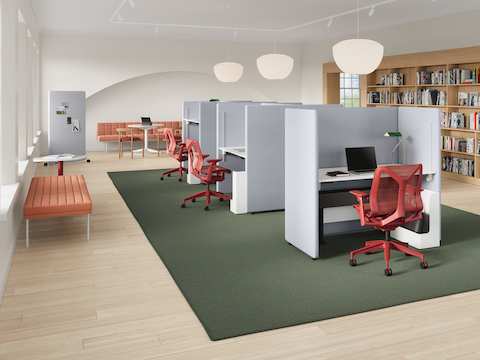 A library setting with grey Bound Sit-Stand Desking and a Bound Sit-Stand Booth at the end of the configuration, shown with red Cosm chairs, with a Bound Mobile Screen in the background.