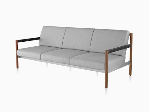 Un divano Brabo con imbottiture grigio chiaro, pelle, dettagli metallici e telaio in legno a vista. Vista da un angolo.
